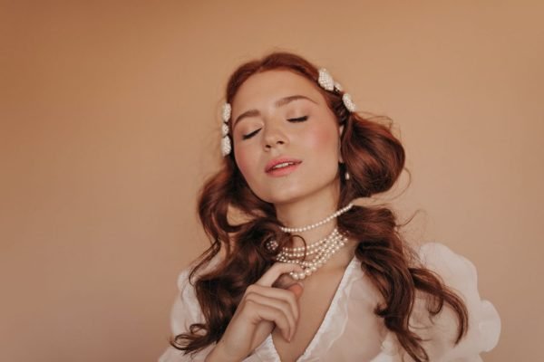 girl-in-light-blouse-poses-on-beige-background-woman-touching-her-pearl-beads.jpg